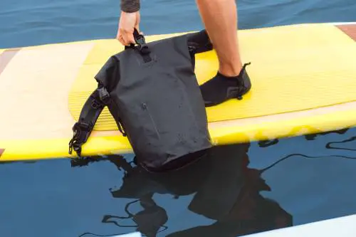 man-on-surfboard-holding-a-black-waterproof-rucksack