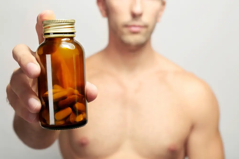 A muscular man holds a bottle of supplement pills.
